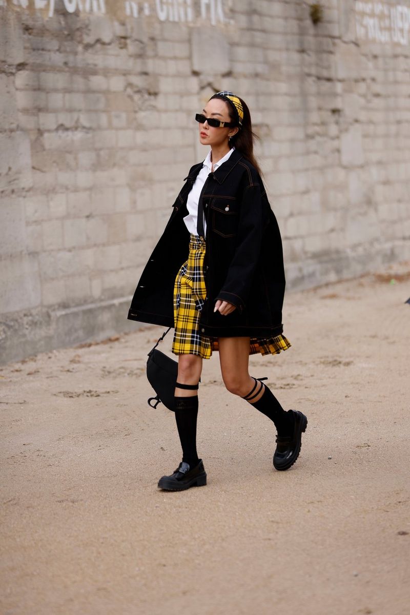 A woman wearing a black jacket, yellow and black chequered skirt and sunglasses walks down the street. Taken on a Canon EOS R5 by fashion photographer Leo Faria.