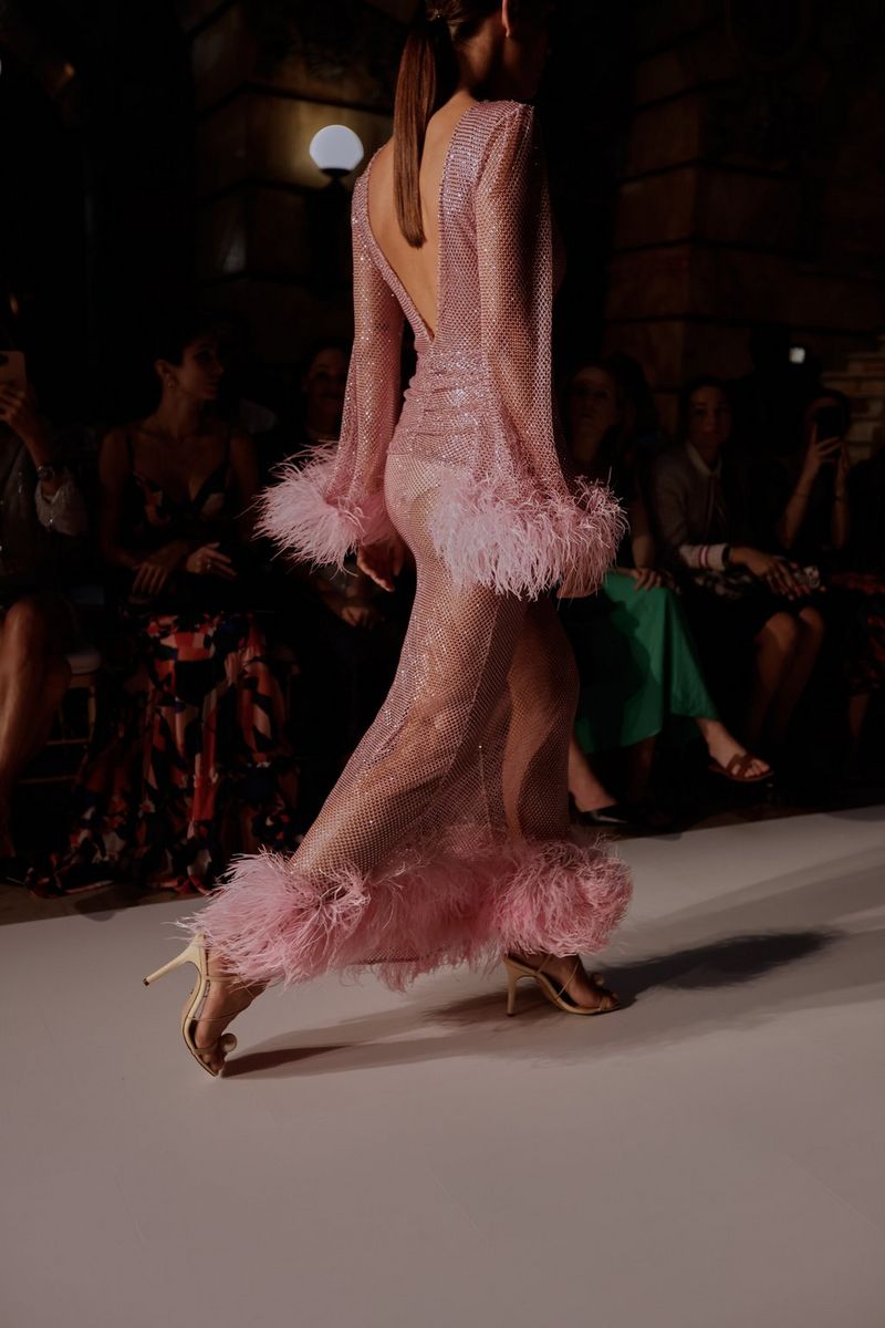 A model walking the runway in a long pink sequinned dress with a feather trim. Taken by fashion photographer Leo Faria using the Canon EOS R5. 
