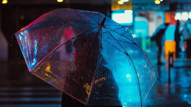 A woman under a clear plastic umbrella crosses a road in Tokyo at night. 