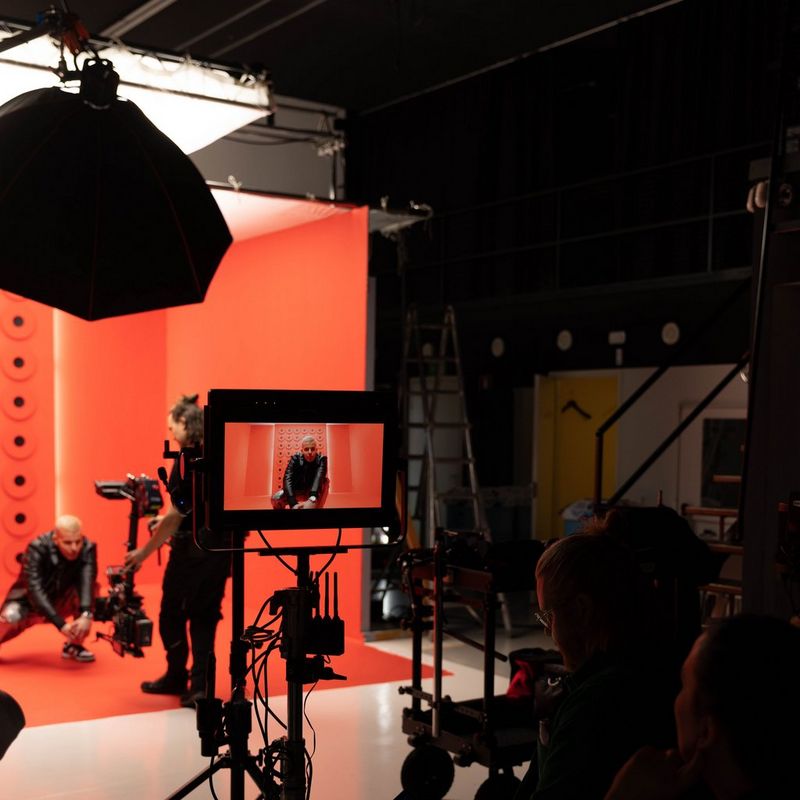 Человек присел перед камерой Canon на красном фоне — его можно увидеть на экране на переднем плане снимка.