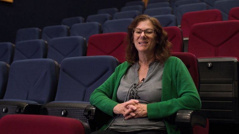 A woman in a green cardigan sitting in a lecture hall.