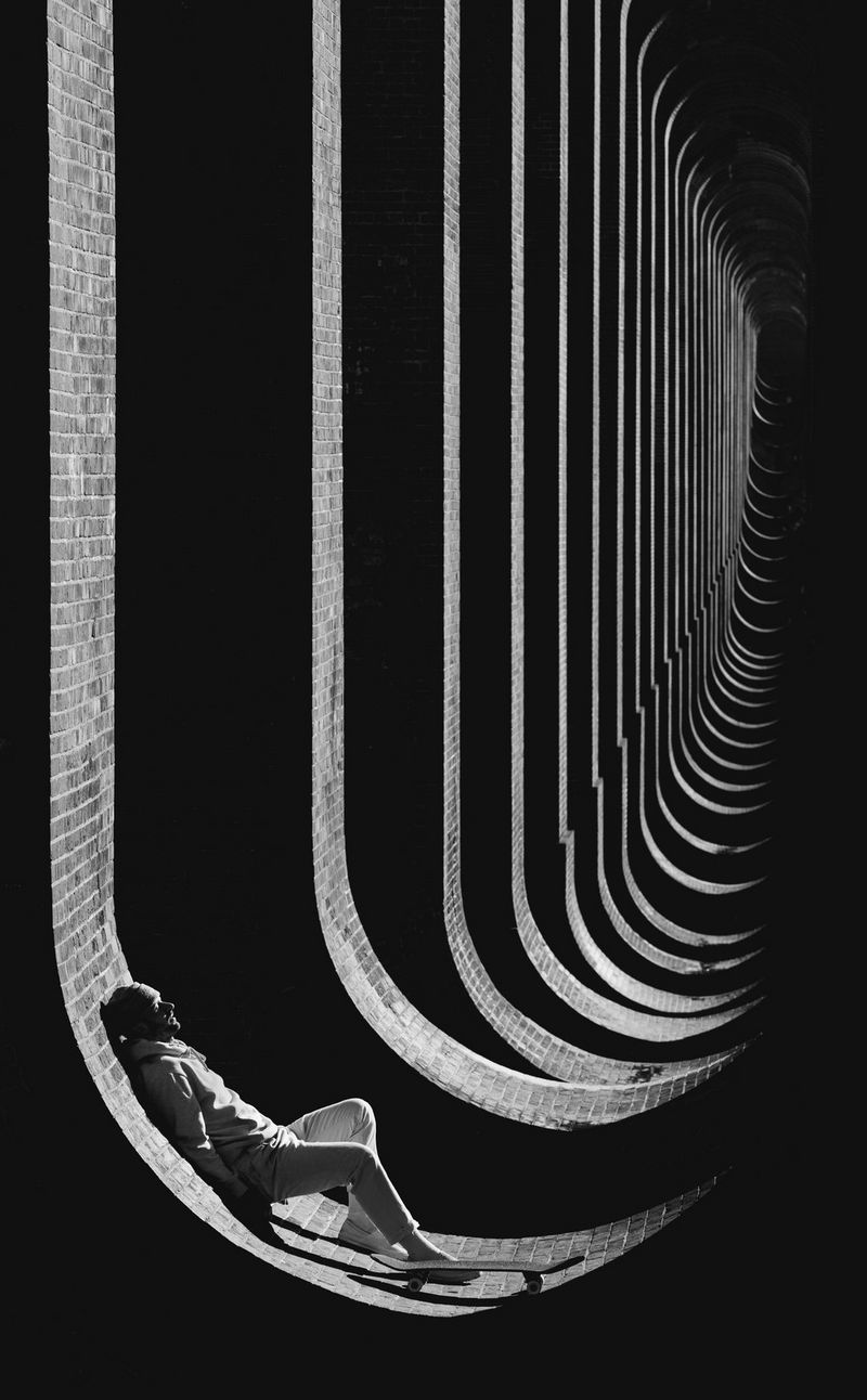 A skateboarder leans against the curved wall of a viaduct base.