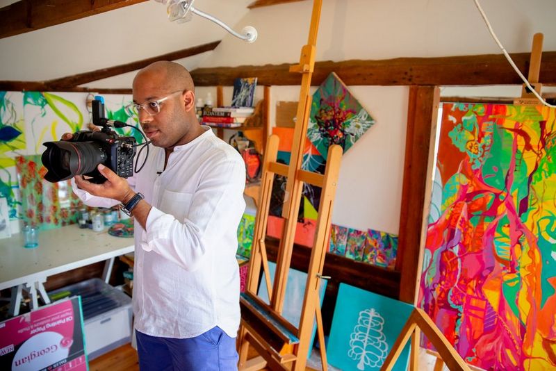 Filmmaker Simeon Quarrie filming in an art studio in front of a large easel with a Canon EOS C70 camera .