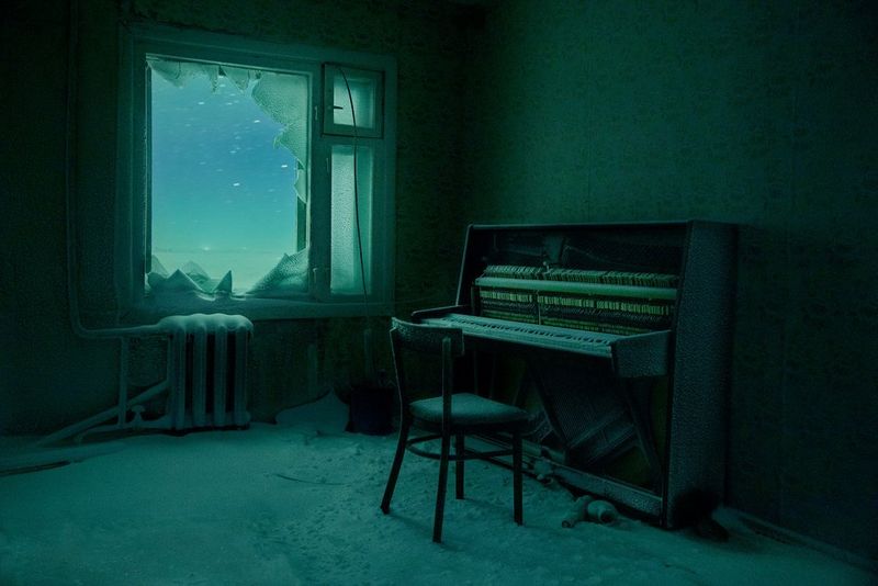 An abandoned room with a piano, the floor covered in snow. The light of the Aurora Borealis can be seen through the shattered window.