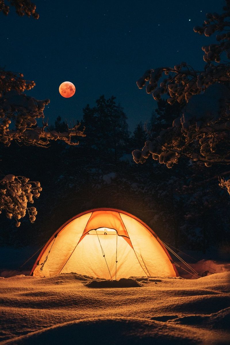 Een volle bloedmaan aan de nachtelijke hemel boven een halfronde tent die van binnenuit wordt verlicht.