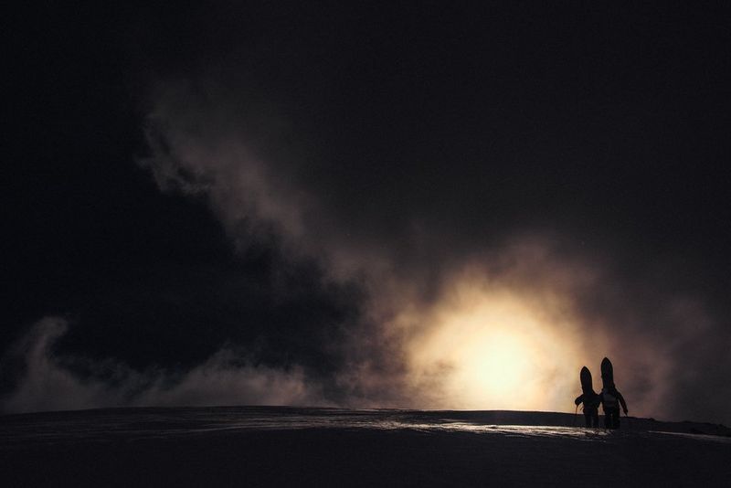 Twee wandelaars waarvan je het silhouet ziet tegen een felle cirkel zonlicht dat door donkere stormwolken schijnt.