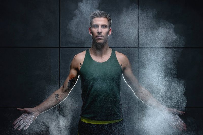 Легкоатлет Марцин Левандовский стоит в зеленой майке среди облака магнезии, раскинув руки.