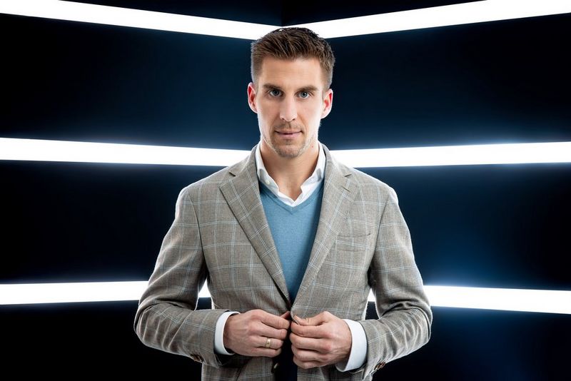 Легкоатлет Марцин Левандовский в синем свитере и светло-серой куртке позирует на камеру в небольшой комнате, залитой контровым светом.