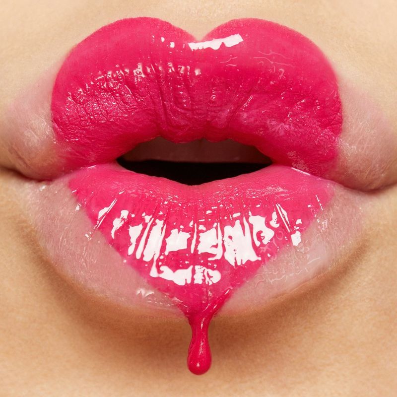 A close-up of a pouting pair of lips, with a heart shape drawn on in bright pink gloss and dripping from the point at the bottom, by macro photographer Tina Eisen.
