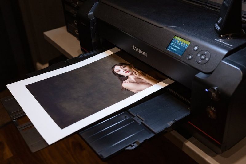 A Canon imagePROGRAF PRO-1000 printer with a large print of a photograph of a woman with long dark hair on the out tray.