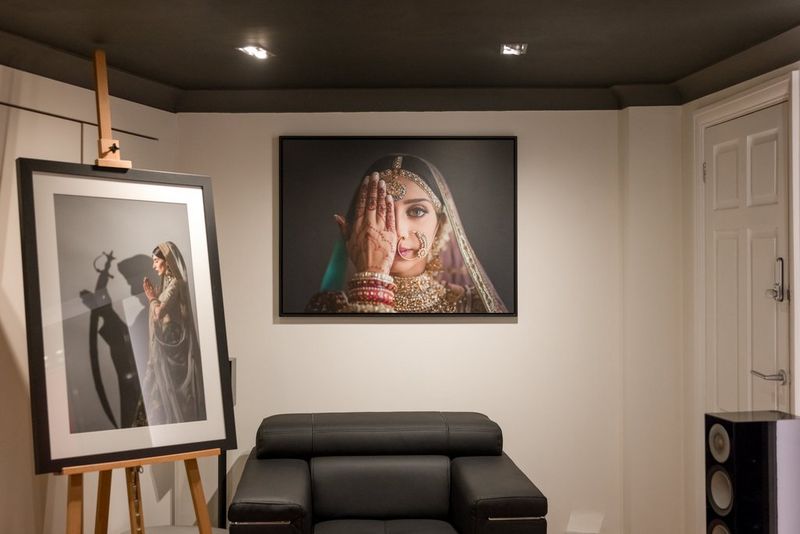 A small white showroom, with a comfortable black armchair in the middle, a large print on the wall behind and a framed print on an easel to the side.