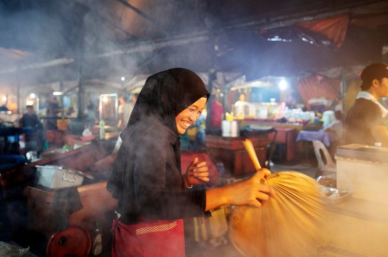 Een vrouw staat in een overdekte markt; ze lacht en veegt een oppervlak schoon.