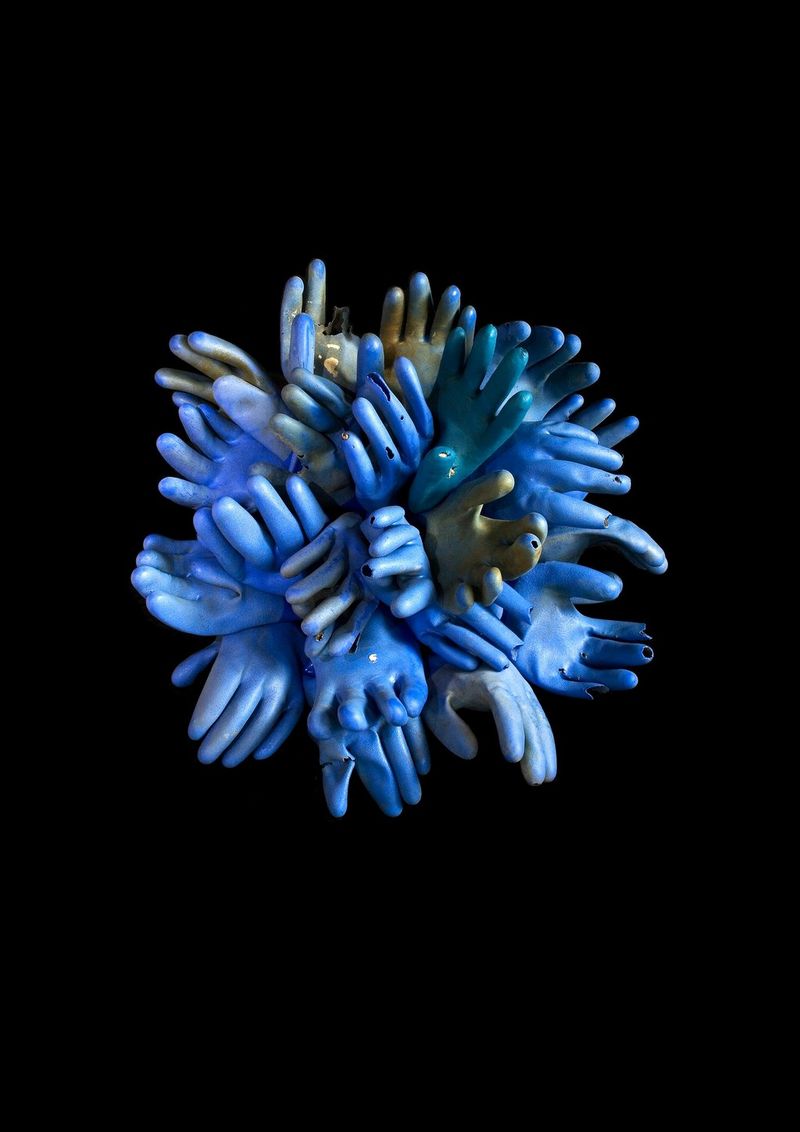 A cluster of blue PVC gloves, arranged to resemble coral, pictured against a black background.