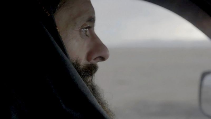 A still from In Her Hands showing a close-up of a man's side profile as he sits in a car and looks ahead, filmed by Marcel Mettelsiefen.