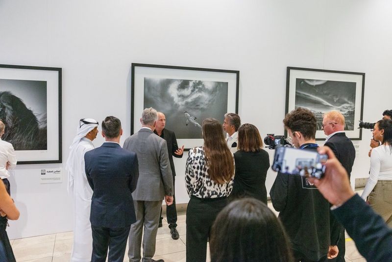 Chris Fallows, fotografo naturalista, è ritratto davanti a una parete tappezzata di sue stampe in grande formato all'aeroporto di Dubai, mentre parla a una folla di visitatori.