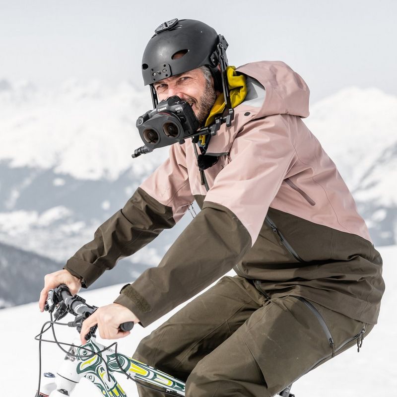 A man on a bicycle on a snowy mountain with a helmet on his head and a VR headset on his face