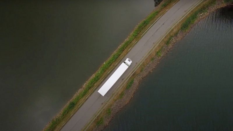 Veduta aerea di un grande autocarro che percorre una lunga strada circondata dall'acqua.