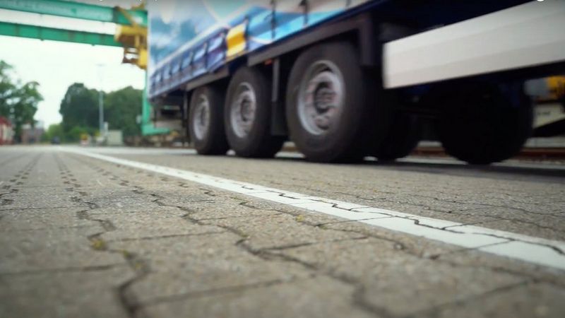 Un primo piano dal basso delle ruote di un grande camion che entra in un'area industriale.