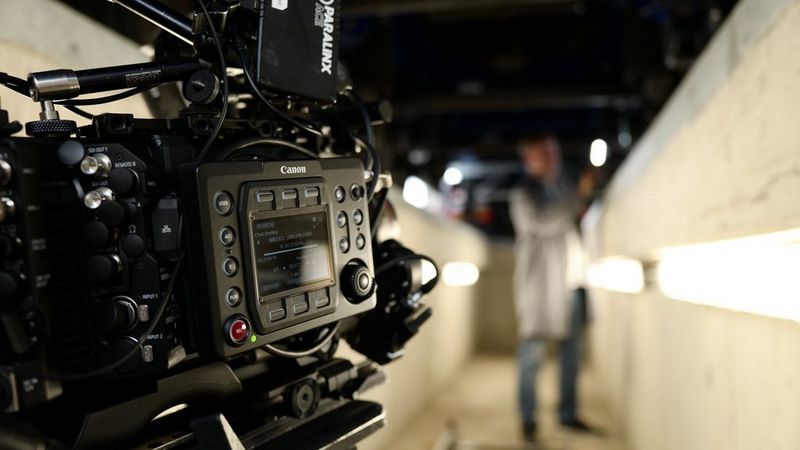 Primo piano di una fotocamera Canon che riprende un uomo in piedi accanto a un muretto illuminato da strisce luminose.