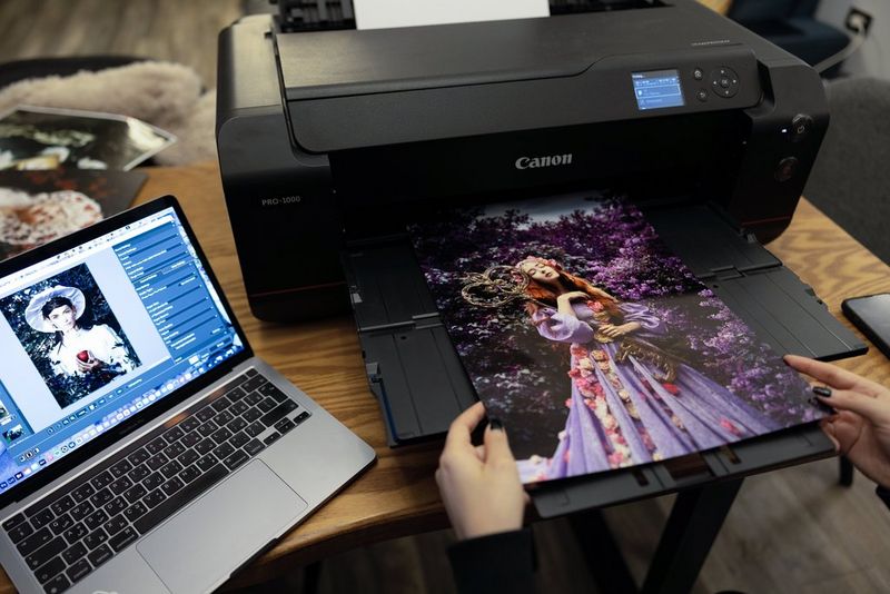 Menna Hossam tient une impression d'une femme vêtue d'une robe violette enlaçant une clé géante, éjectée d'une Canon imagePROGRAF PRO-1000. Un ordinateur portable est installé à côté de l'imprimante.