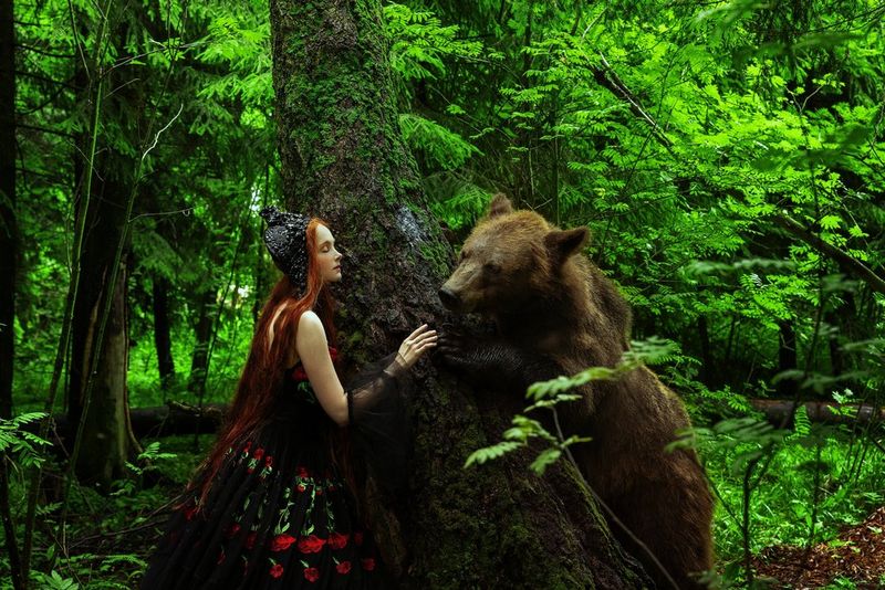 Une femme se tient près d'un arbre et tend la main vers un ours marron. Photo prise par Menna Hossam avec un Canon EOS R5.