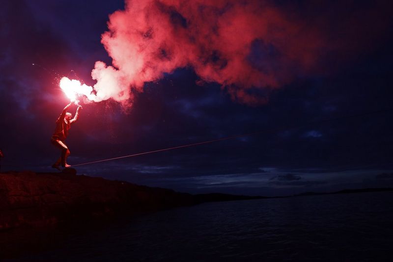 A slackline walker holds a blazing torch overhead with both hands.