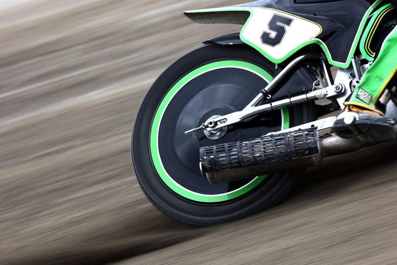 The rear wheel of a bright green speedway bike mid-race.