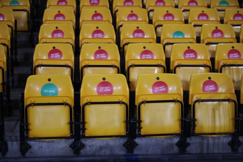 A bank of closed seats in a football stadium, with a few marked "sit here" amongst a far greater number marked "do not sit here".