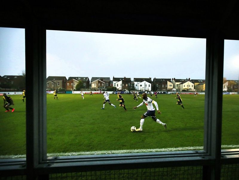 A footballer in a white shirt and black shorts runs with the ball in an image framed by the barrier the photographer is sitting behind.