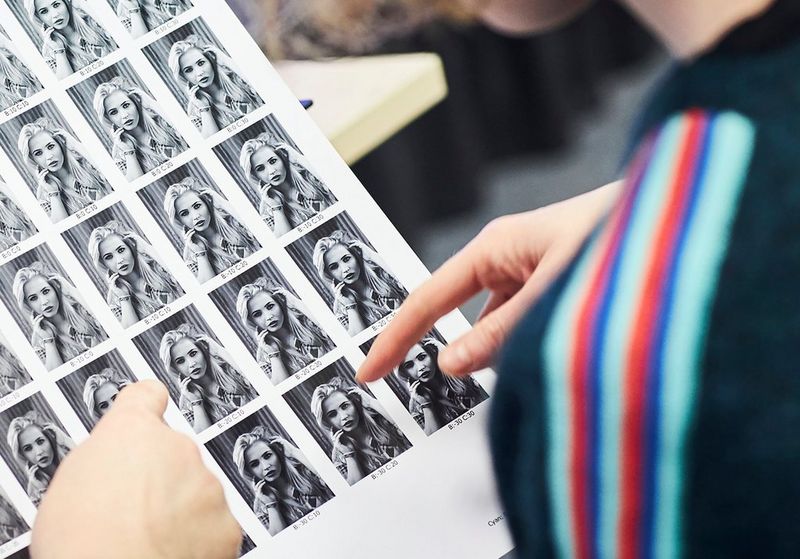 Photographer Helen Bartlett scrutinises a printed contact sheet of thumbnails of one of her black and white photos, each thumbnail showing a different combination of print settings.