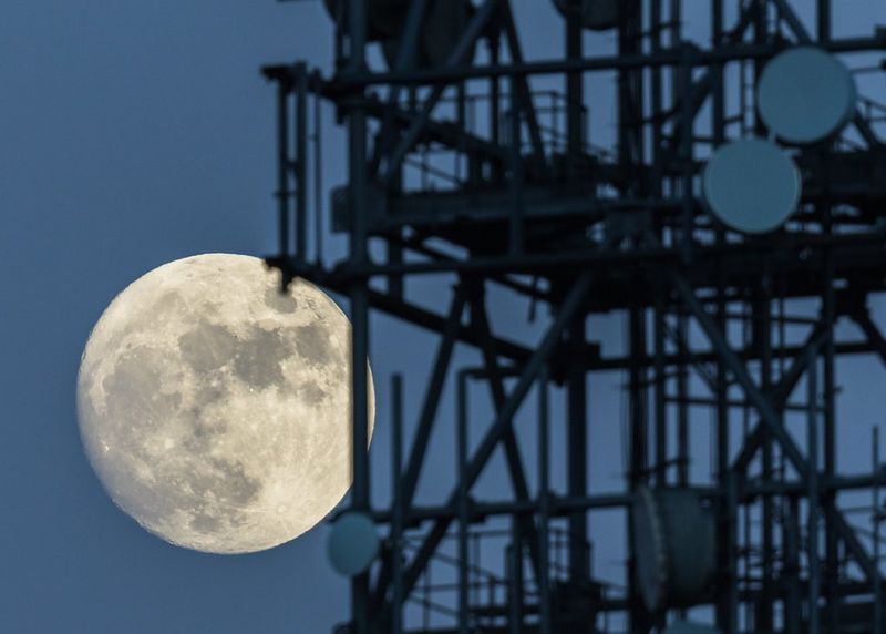 Полная луна за радиолокационной станцией и телефонной вышкой на холме Титтерстоун-Кли в графстве Шропшир.