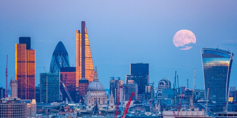 На фотографии, сделанной Джеймсом Бернсом, над городским пейзажем Лондона возвышается Луна в белых тонах.