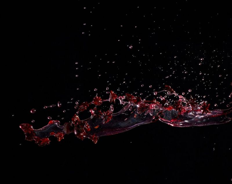 Cherry syrup and star anise captured mid-splatter against a black background.