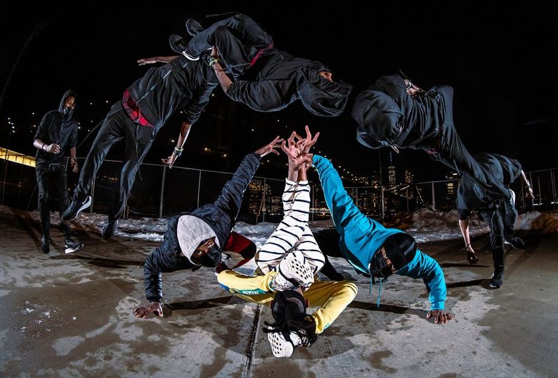 Photo à exposition multiple de trois hommes masqués faisant du break dance, tandis qu'un autre fait un saut acrobatique au-dessus d'eux, prise avec un Canon EOS R6 par Josh Katz.