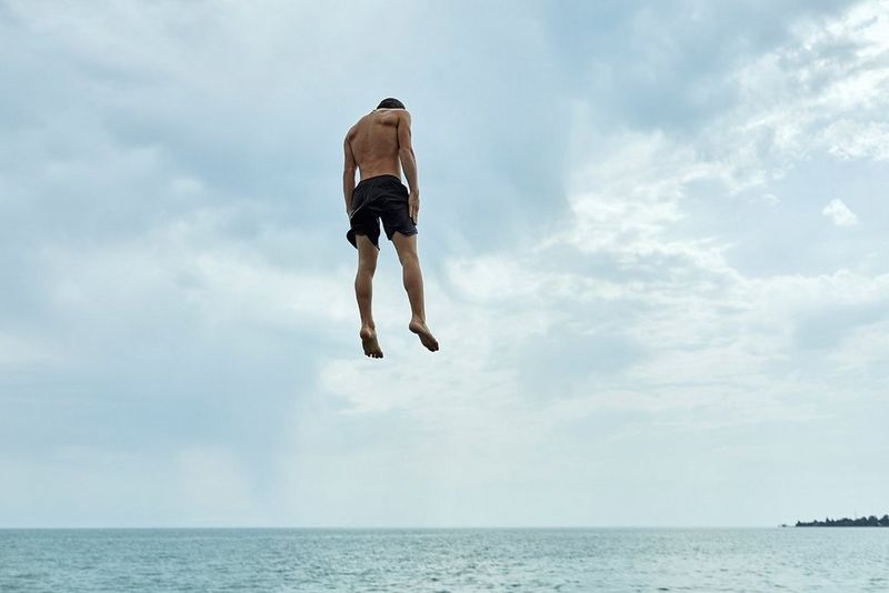 A boy appears to be suspended in the air as he jumps from a pier into the sea. 