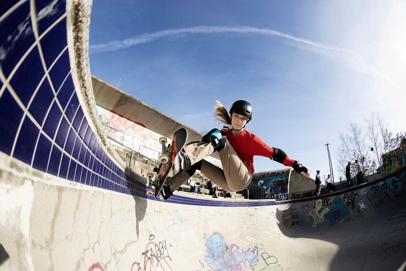 A girl skateboarding, at the apex of a curved, graffiti-covered ramp, approaching the camera.
