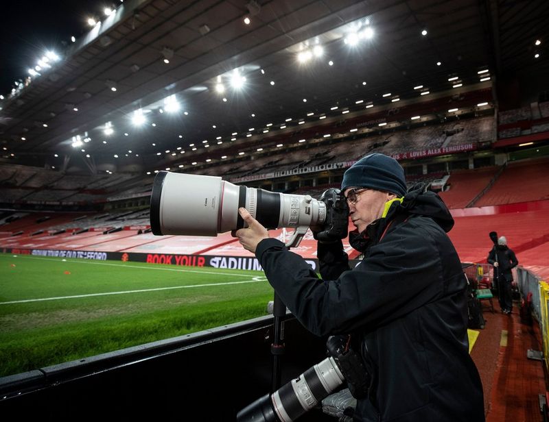 Eddie Keogh houdt in een sportstadion een camera met daarop een groot objectief vast. Hij heeft een andere camera met objectief om zijn nek hangen.