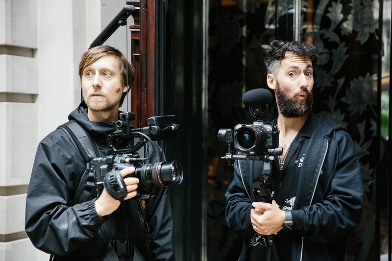 מפעיל מצלמת Canon Cinema EOS במתקן EasyRig ואדם נוסף מחזיק גימבל עם מצלמת Canon קטנה יותר שאליה מחובר מיקרופון חיצוני.