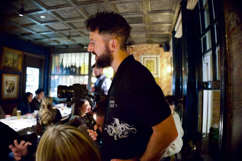 A camera operator with a Canon camera on a gimbal on a shoot in a dimly-lit function room.