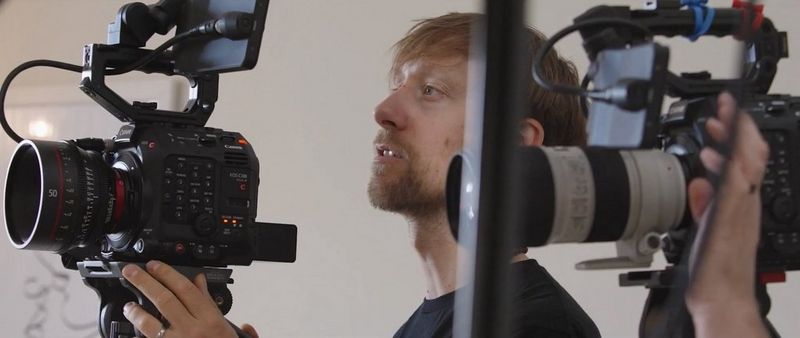 A camera operator watches the monitor screen attached to a Canon EOS C300 Mark III, with another Canon camera out of focus in the foreground.