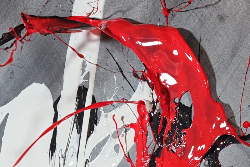 Red and white paint being thrown through the air onto a grey sheet. 