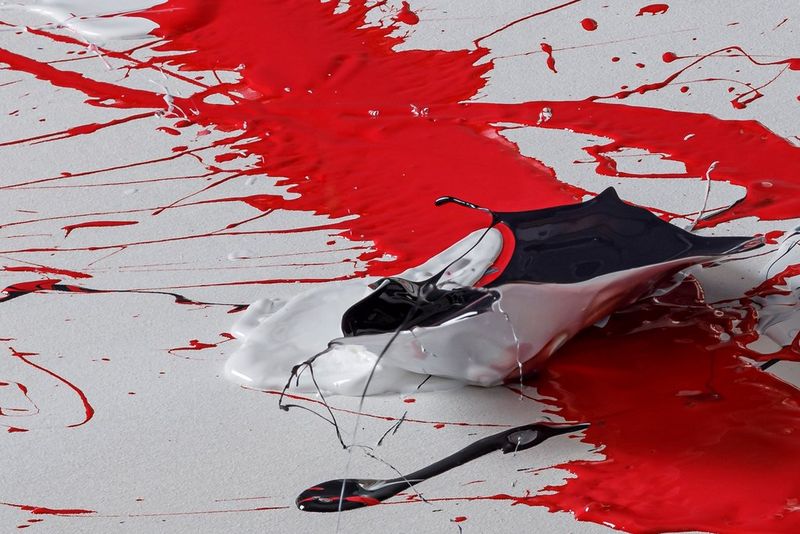 A splash of red paint is splattered with black and white paint.  
