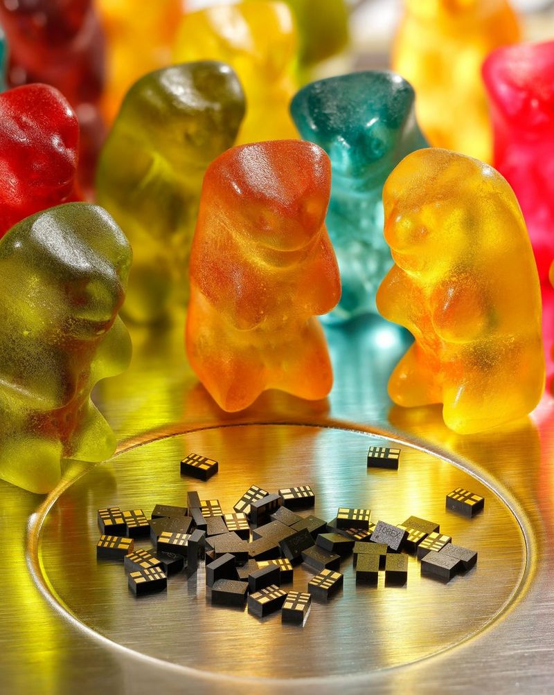 Een stel helder gekleurde gummibeertjes rond een glazen schaal met miniscule dominostenen