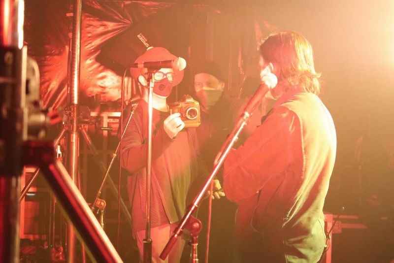 Cinematograaf Anthony Dod Mantle filmt een bandlid met een Canon EOS-1D X Mark III op een podium met rood en geel licht.