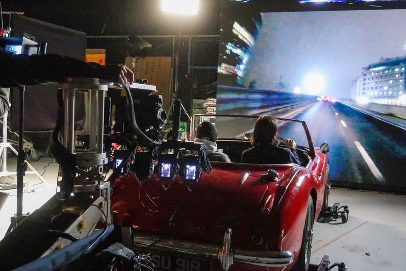 Een serie Canon EOS R5-camera's filmt twee mensen van achteren in een auto in de jaren zeventig. Op een scherm op de achtergrond is een levendige Londense straat te zien.