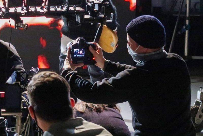 Een gemaskeerde crewmember filmt met een Canon EOS-1D X Mark III-camera op een donkere filmset. Verschillende andere crewmembers kijken toe.