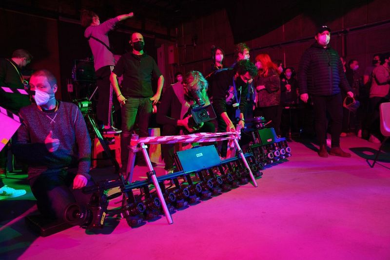 Een persoon filmt met een Canon XL H1 op een filmset die baadt in roze licht. Voor hem liggen twee bar cams met achttien Canon EOS R5-camera's.