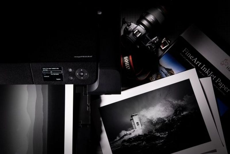 A Canon camera next to a Canon printer and a selection of black and white prints. 