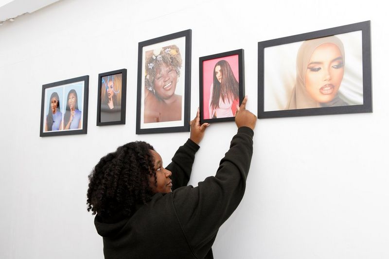 Fashion photographer Jade Keshia Gordon hangs a framed photo, printed by a Canon PIXMA printer, on a white wall. Four other framed photos also hang on the wall. 