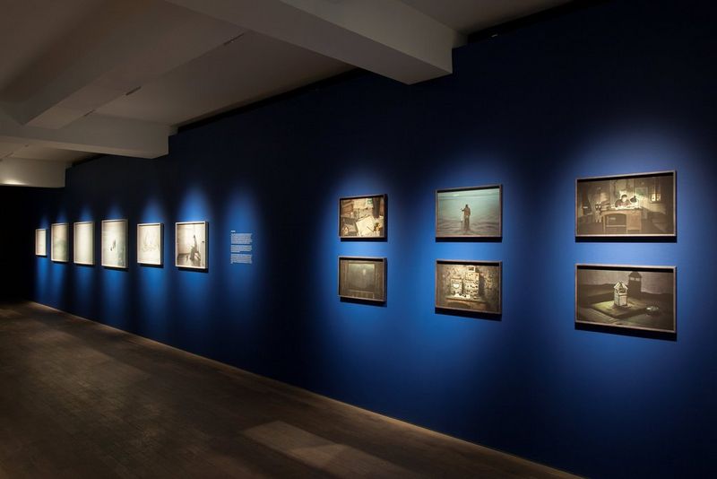 Photographs mounted on the blue walls of a large exhibition space.